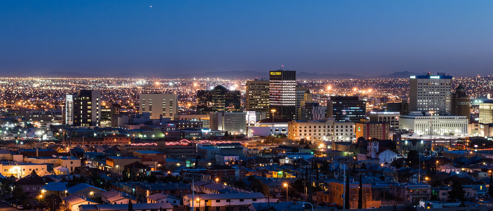 The city of El Paso is looking lively & lit up at night, covered by the bright blue sky.