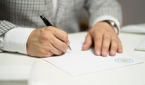 Man in a checked blazer signing a white paper document